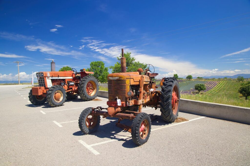 Two vintage tractors parked outdoors with fields and blue sky background.