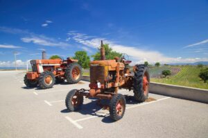 Two vintage tractors parked outdoors with fields and blue sky background.