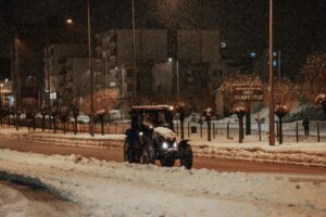 A lone tractor plows a snow-covered street at night in the city.