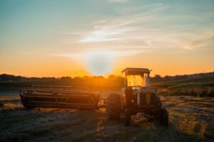 A serene rural scene with a tractor in a field during a vibrant sunset.