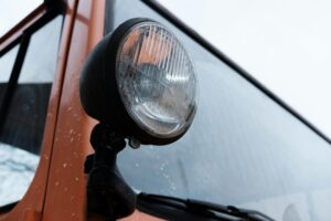 Detailed close-up of a vintage vehicle headlight with raindrops on orange exterior.