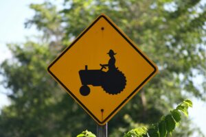 Close-up of a yellow tractor crossing sign on a rural road, set against a lush green backdrop.